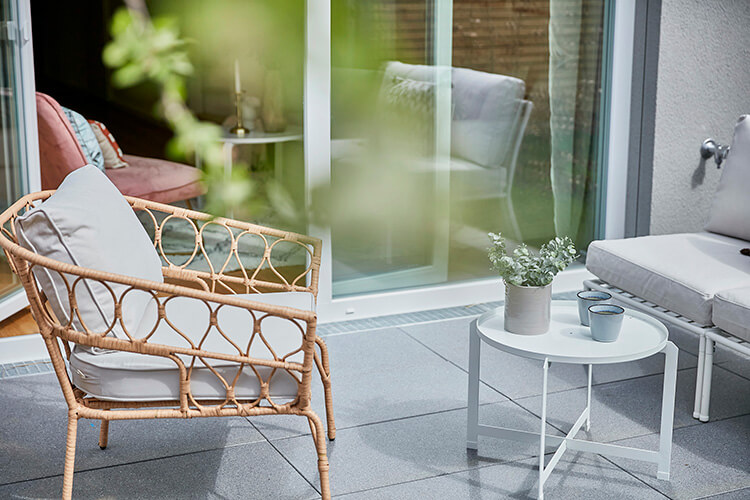Blick von der Terrasse ins Wohnzimmer einer Musterwohnung des Neubauprojektes Constanze. Im Vordergrund stehen ein Korbstuhl und ein kleiner Tisch.