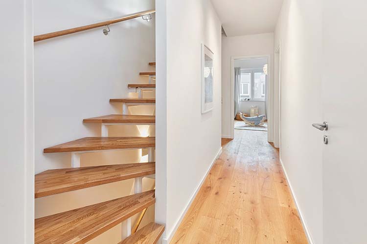Foto des Flurs und der Treppe nach oben in der Musterwohnung des Neubauprojektes Constanze. Weiße Wände mit Parketboden.